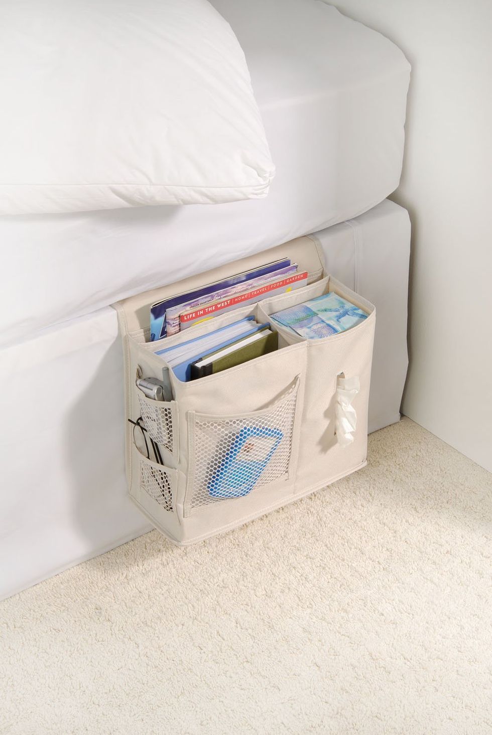 A bedside caddy attached to a bed full of books and magazines.