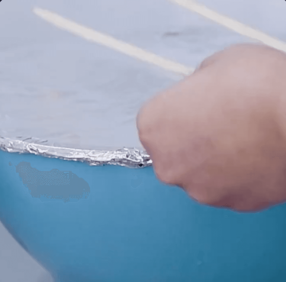A bowl covered in tinfoil with the foil closely folded over at the edges