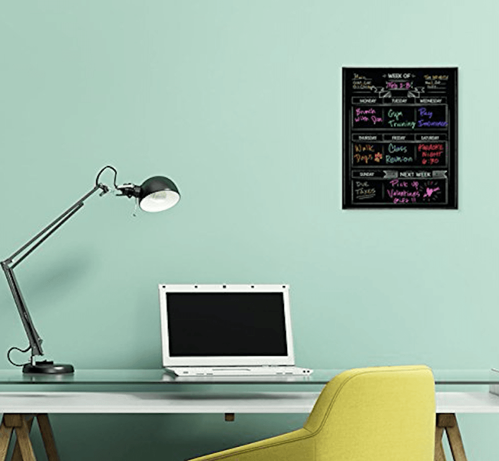 A desk with a laptop and light on it with a dry erase board above the desk.