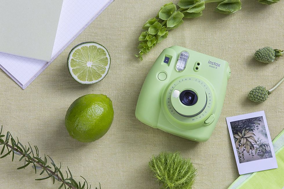 A green instant camera surrounded by other green items including limes and leaves.