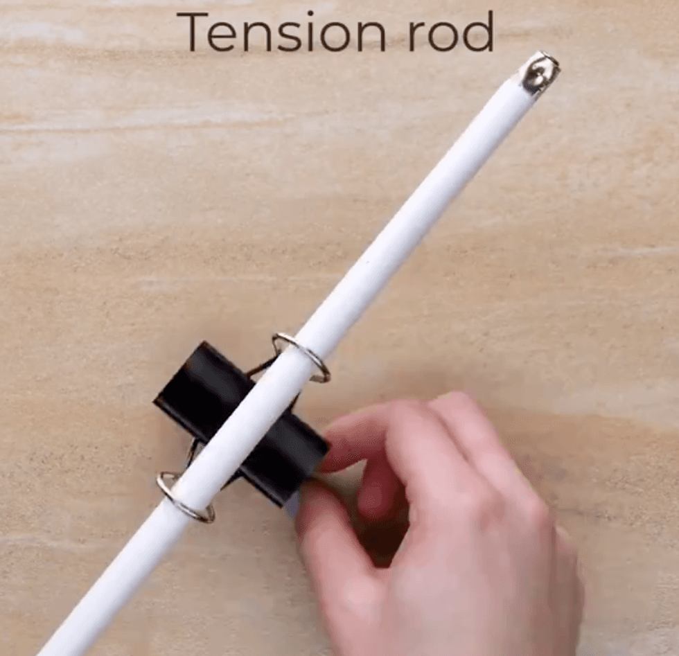 A tension rod has been pushed through the metal ends of a binder clip