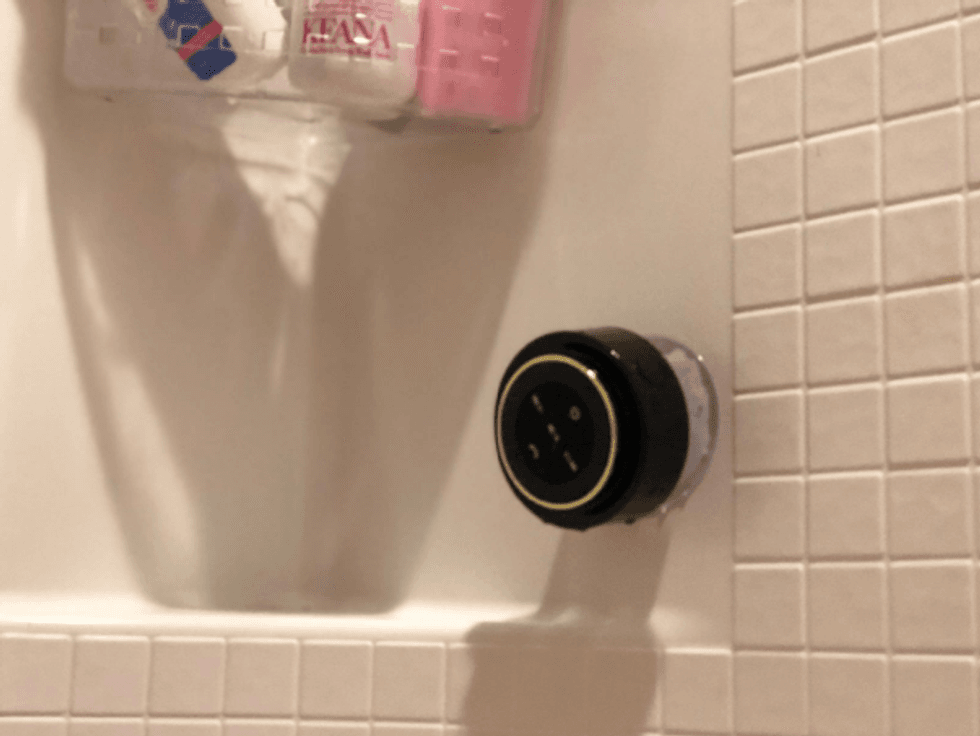 A waterproof bluetooth speaker stuck on a wall in a shower.