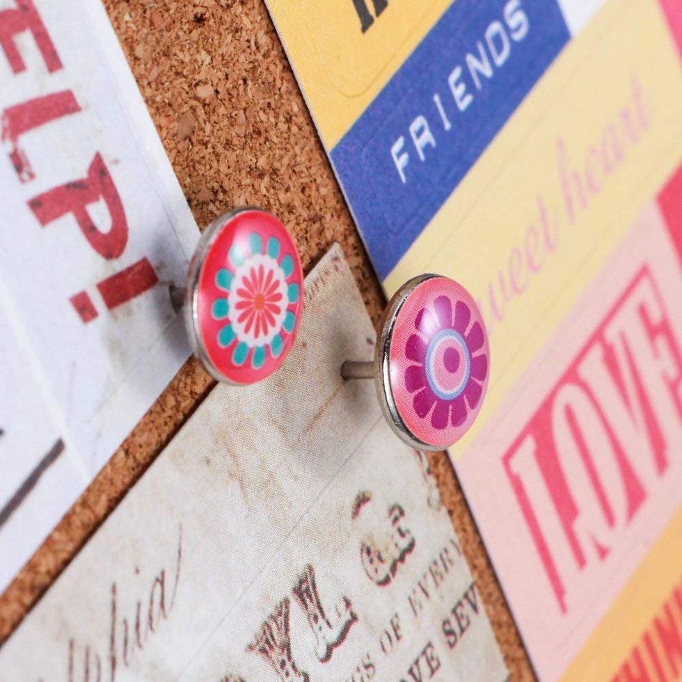 Push pins wit flower designs holding papers on a cork board.